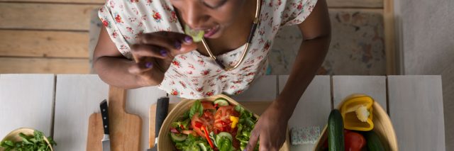 An African American woman eating a salad at a table, with the camera looking down at her.
