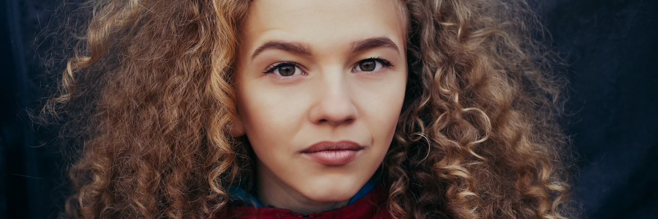 Close-up portrait of girl with long curly blond hair on black background