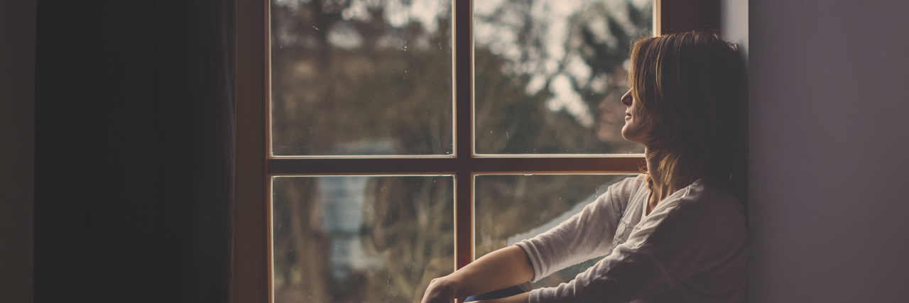 8 Takeaways From Being Hospitalized for My Mental Health Young attractive woman, sitting on a window, looking outside, lonely mood