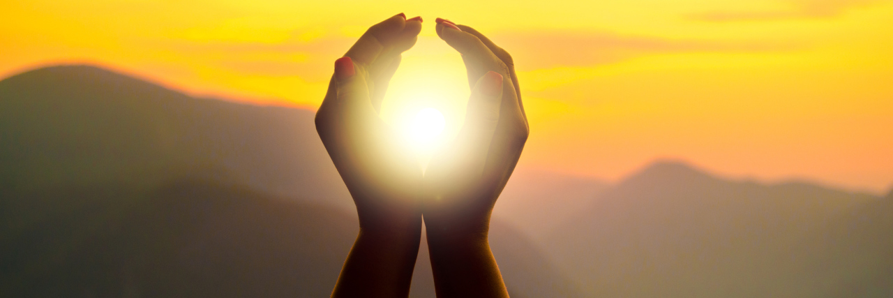 Woman's hands circling the sun, during a sunset in the mountains.