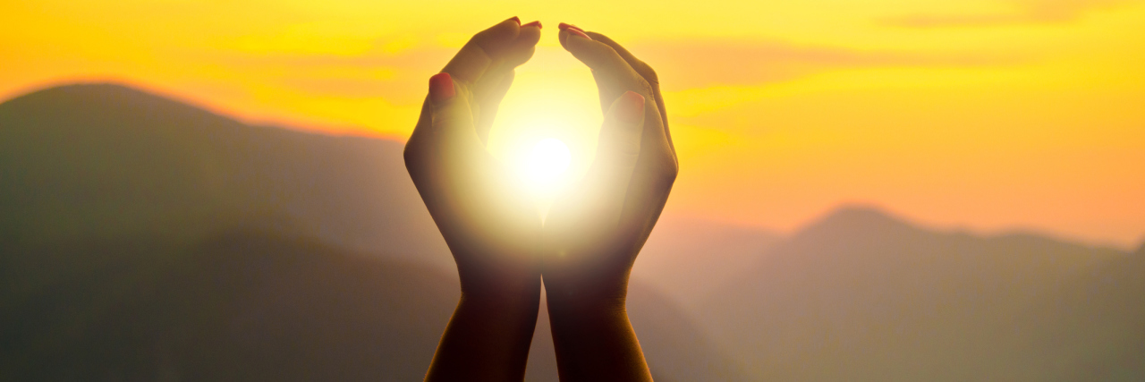 What Chronic Pain Demands Woman's hands circling the sun, during a sunset in the mountains.