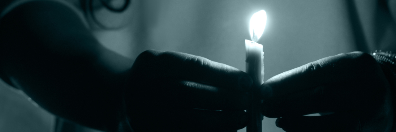 How You and I Can 'Bring Hidradenitis Suppurativa to Light' A woman holding a lit candle in the dark.