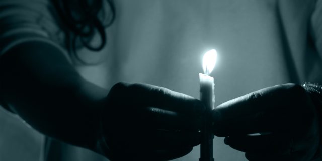 A woman holding a lit candle in the dark.