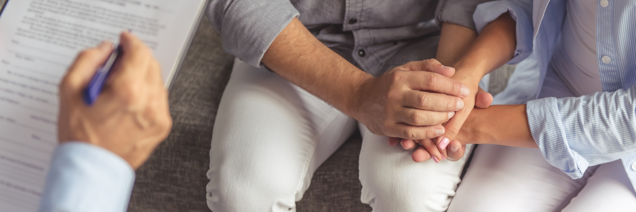 Cropped image of young couple holding hands while sitting on the couch in a doctor's office