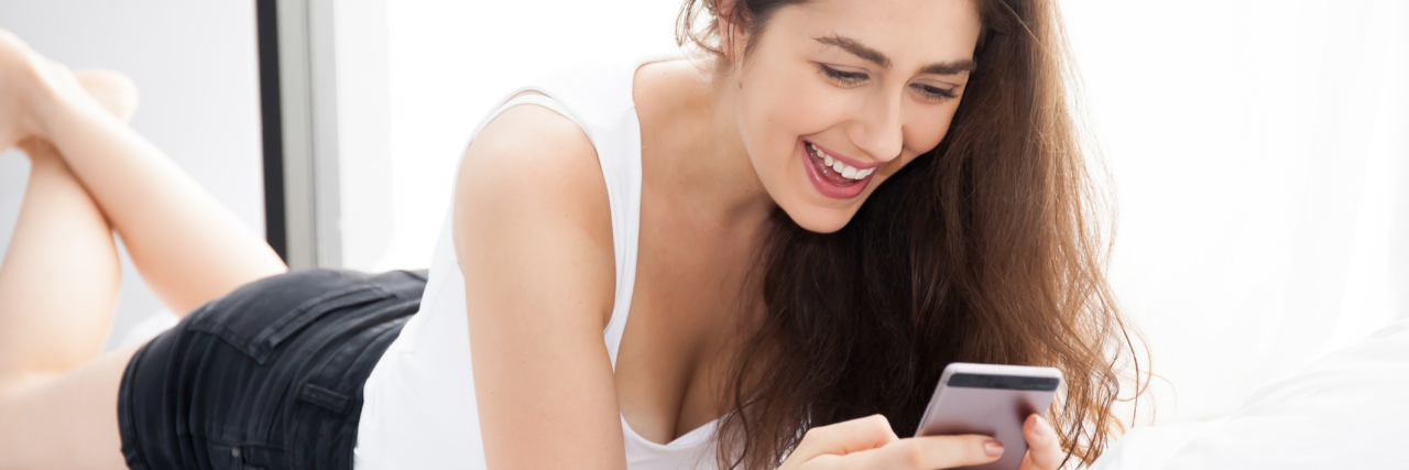 Making Spoonie Friends Through Friendship Dating Apps woman lying in bed on her stomach and texting