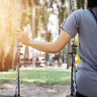 Lonely woman swinging in the park reaching and holding empty swing next to her