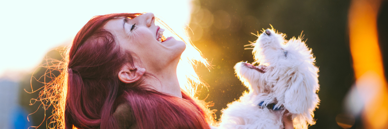 What Makes Dogs Great for Your Mental Health and Wellbeing rdhead girl holding a white puppy, they both seem to be laughing out loud with heads back showing great joy
