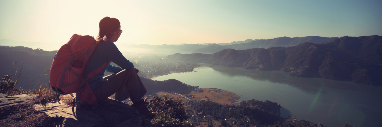 woman wearing a backpack and sitting on the top of a mountain looking at the view