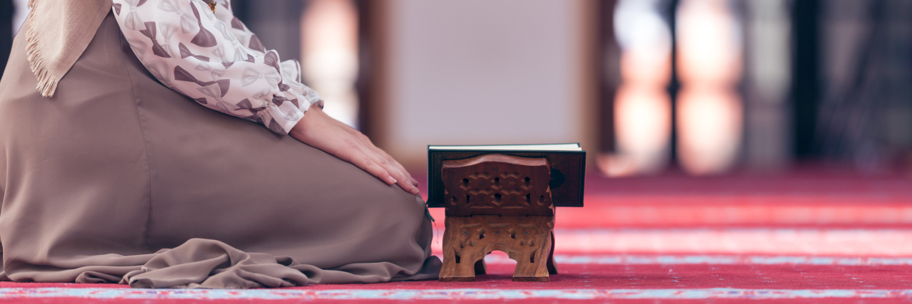 A picture of a Muslim woman kneeling on the ground, reading her Quran.