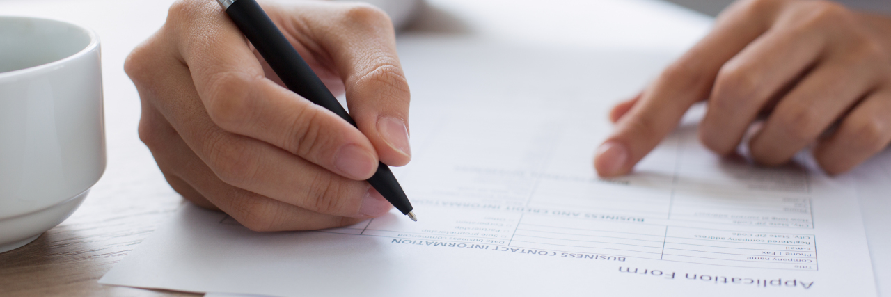 Hiding Autism When Applying for Jobs Woman holding pen and filling out application form.