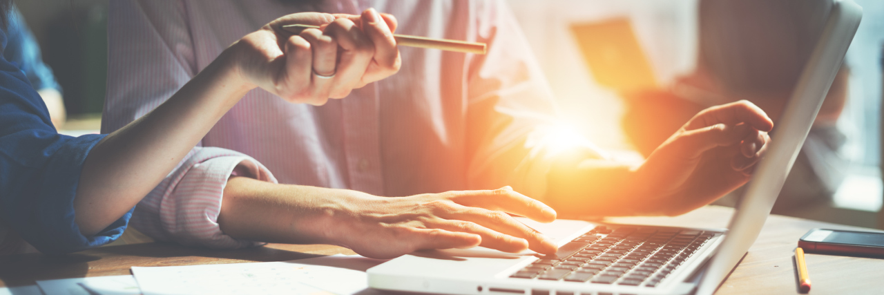 What I Learned When I Asked for Accommodations at Work for My EDS Two people at work that are working on a laptop, with light coming in from a window.