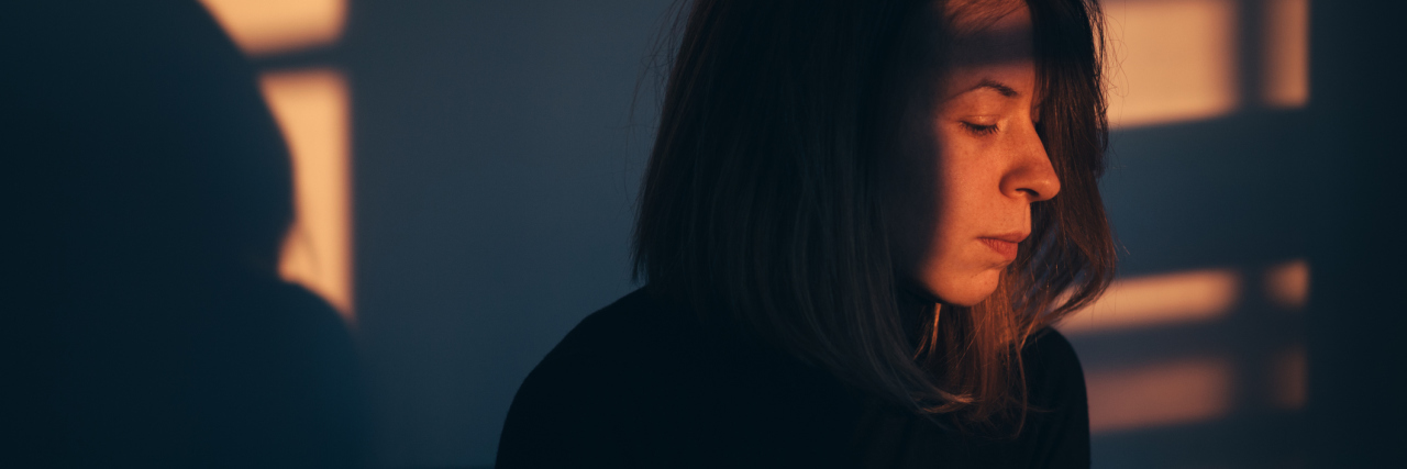 woman sitting alone on her bed illuminated by light coming through the window