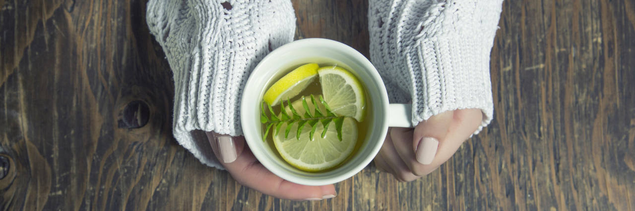 Coping Mechanisms That Help My Mental and Physical Illnesses A woman holding a coffee mug, with tea inside it - as well as thyme herb, and lemon slices.