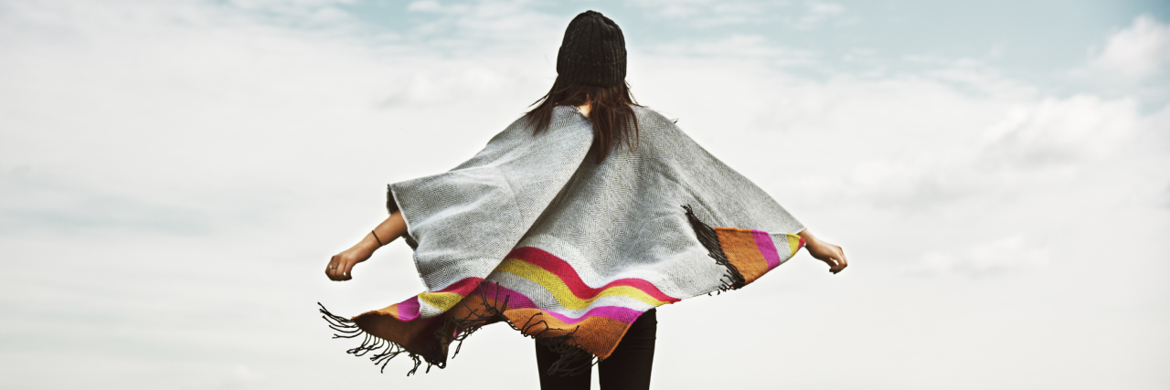 Why I'm OK With What I've Lost Because of Fibromyalgia A woman standing outside with her arms open as the wind blows on her breezy top.