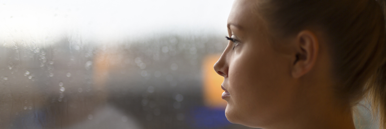 Unemployment Guilt as a Disabled Individual Thoughtful woman looks out the window at home.