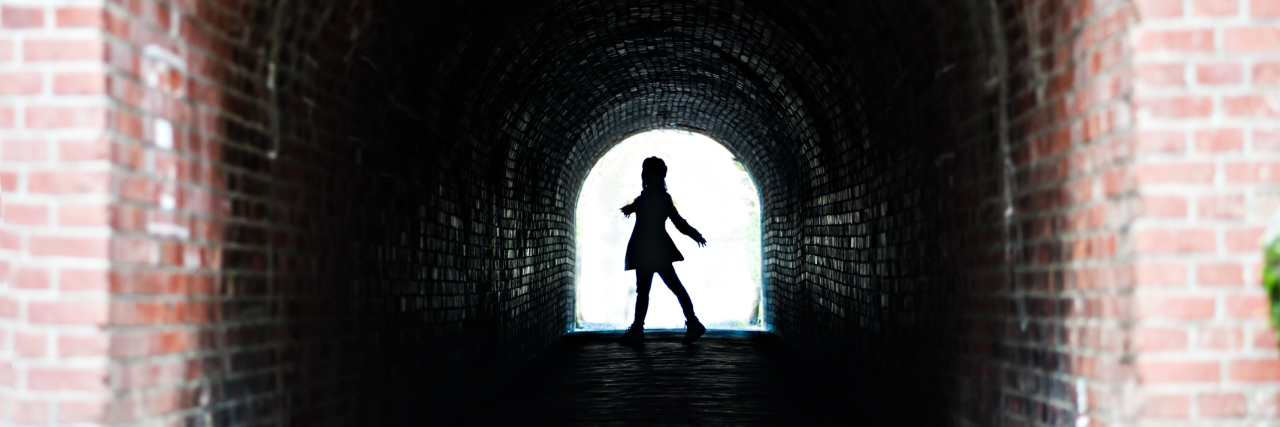 A woman walking by a brick tunnel with a large shadow.