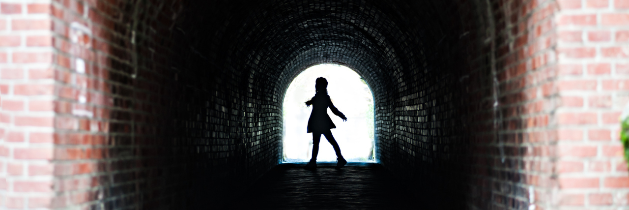 When Multiple Sclerosis Follows You Everywhere A woman walking by a brick tunnel with a large shadow.