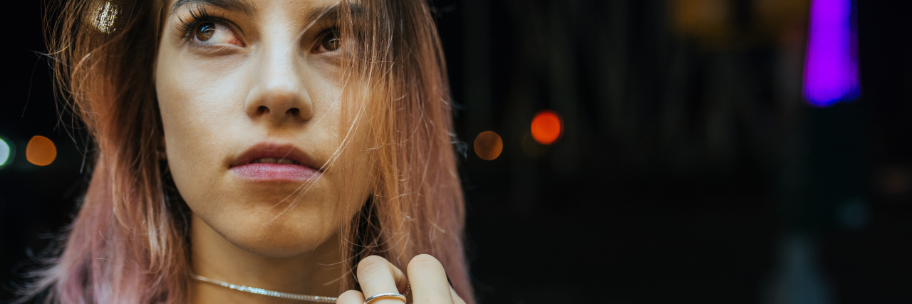 4 Tips on Surviving Chronic Illness in Your 20s A picture of a young woman looking up towards the sky, while playing with her necklace around her neck.