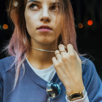 A picture of a young woman looking up towards the sky, while playing with her necklace around her neck.