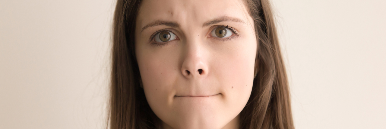 Headshot portrait of indecisive young woman. Beautiful teen girl with pursed lips and worried facial expression looking at camera. Nervous tension, bad feelings and stress. Close up. Front view