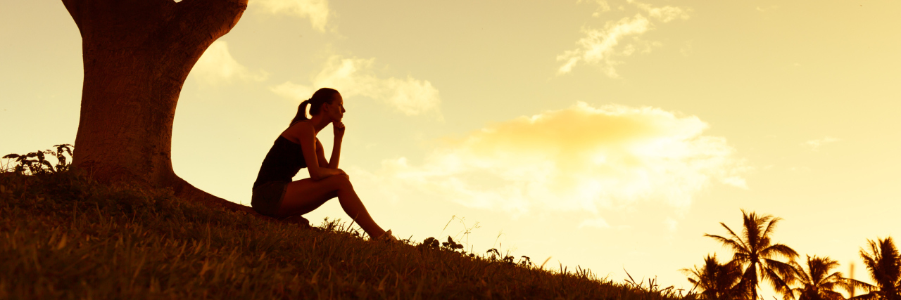When the Death of a Loved One Triggers a Flare-Up of Your Illness woman sitting outside under a tree