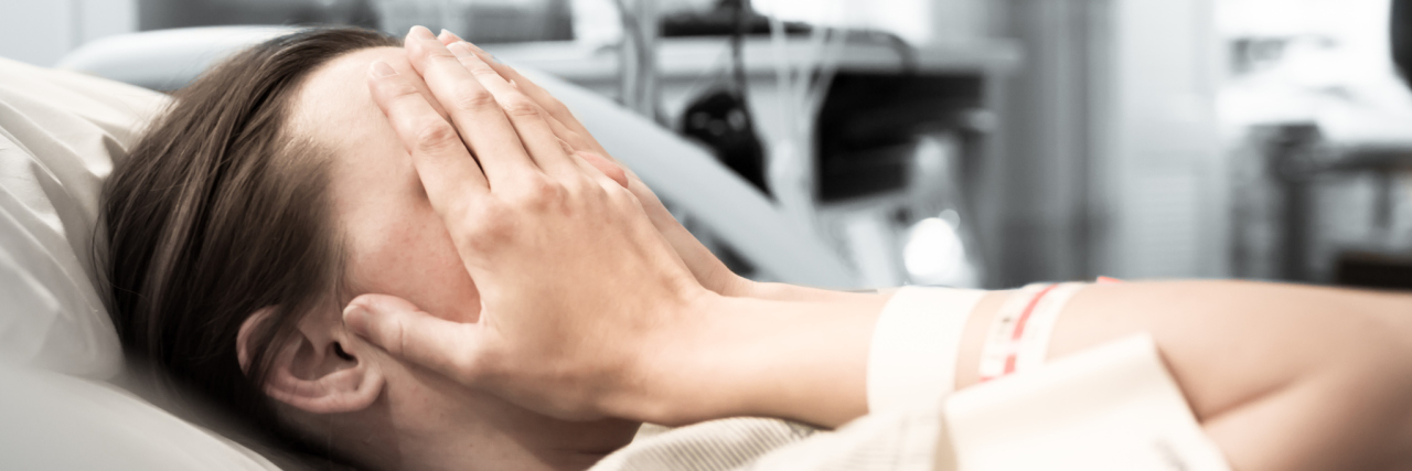 11 of the Toughest Liver Failure Symptoms A young woman laying in a hospital bed with her hands to her face.