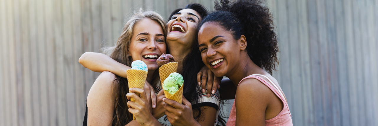 Three girls eating ice cream outside and laughing.
