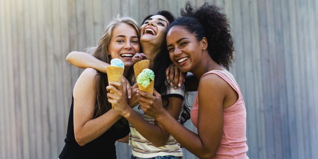 Three girls eating ice cream outside and laughing.