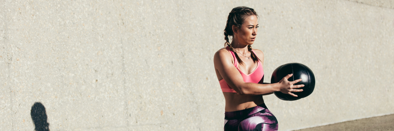 How Exercise Helps Me Cope With Health Challenges woman doing a stretching exercise outside with a medicine ball