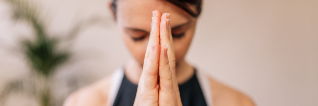 Finding Patience When You're Anxious About Health Issues woman with her hands pressed together breathing and meditating