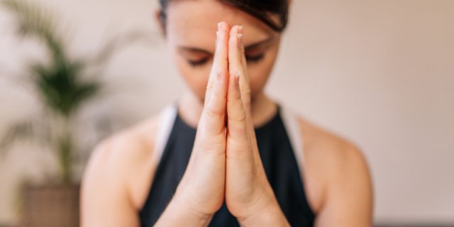 woman with her hands pressed together breathing and meditating