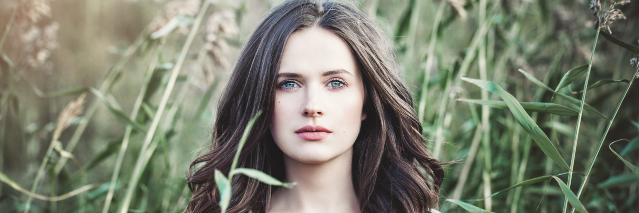 When I Can't Control How Chronic Illness Is Affecting My Body A woman standing outside in a field of long greenery.