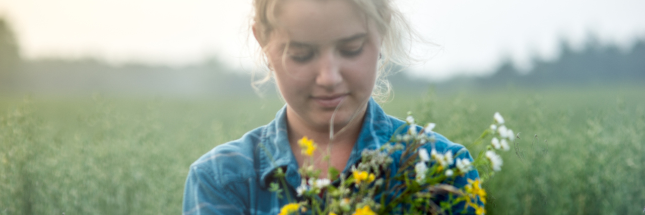 Feeling Better With Chronic Illness After Thanking My Body woman standing in a field holding flowers in her arms