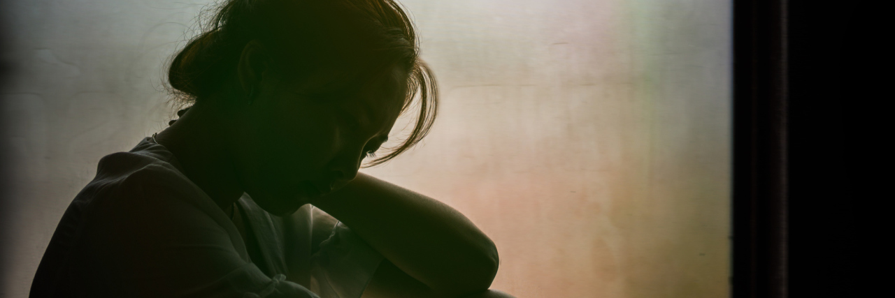 Vintage filtered on silhouette of depressed girl sitting on the window