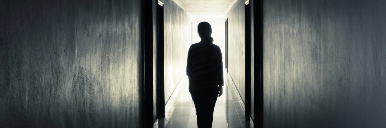 Letting Go of Toxic Family Members When You Have an Illness woman walking down dark hallway towards light