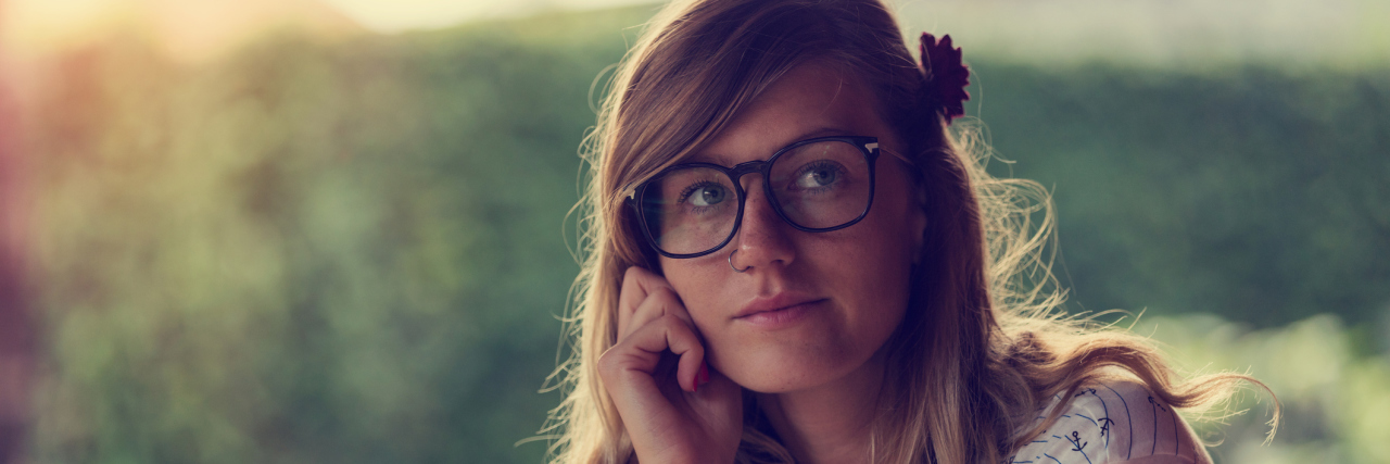 Why I Didn't Realize I've Been Chronically Ill My Whole Life A woman sitting in front of a window, with a green nature background, looking up and thinking.
