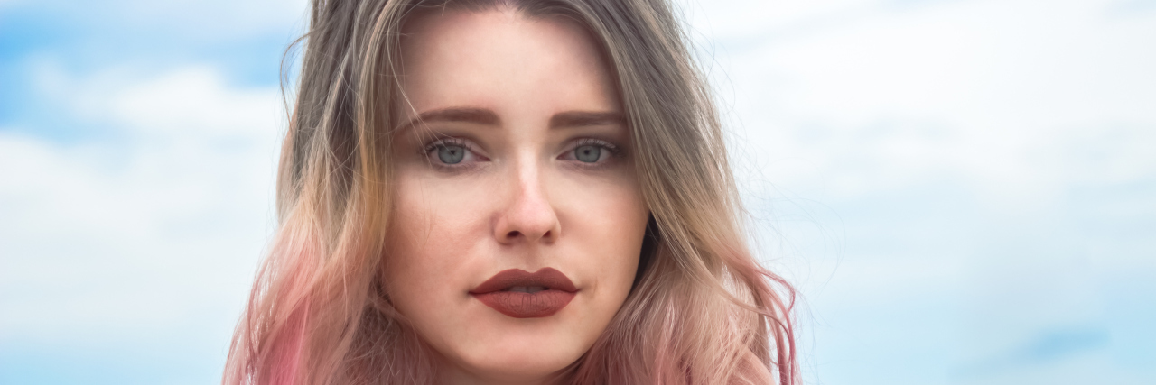 The Autoimmune Disease Guessing Game A woman with colorful hair and a serious expression looking towards the camera while standing outside.