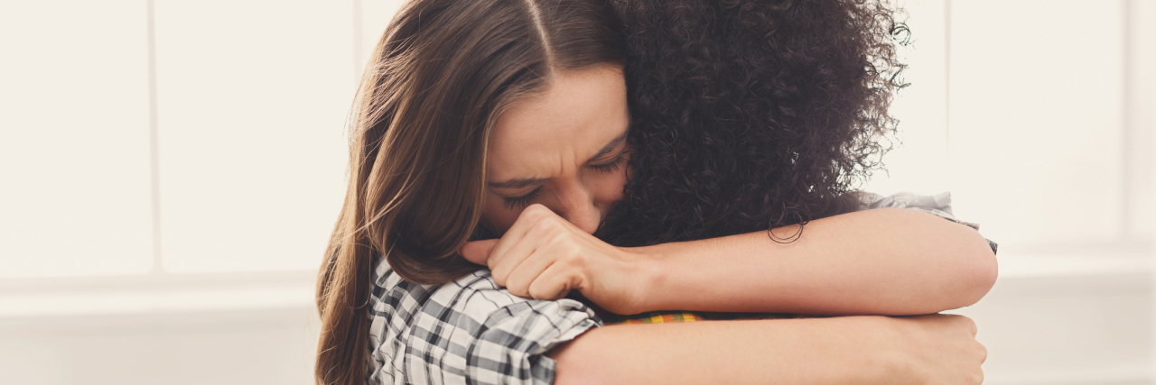 Why I Embraced a Stranger in the Hospital Cafeteria Two women hugging, one holding a tissue in her hand.