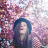 woman wearing a hat and striped shirt laughing under a cherry blossom tree