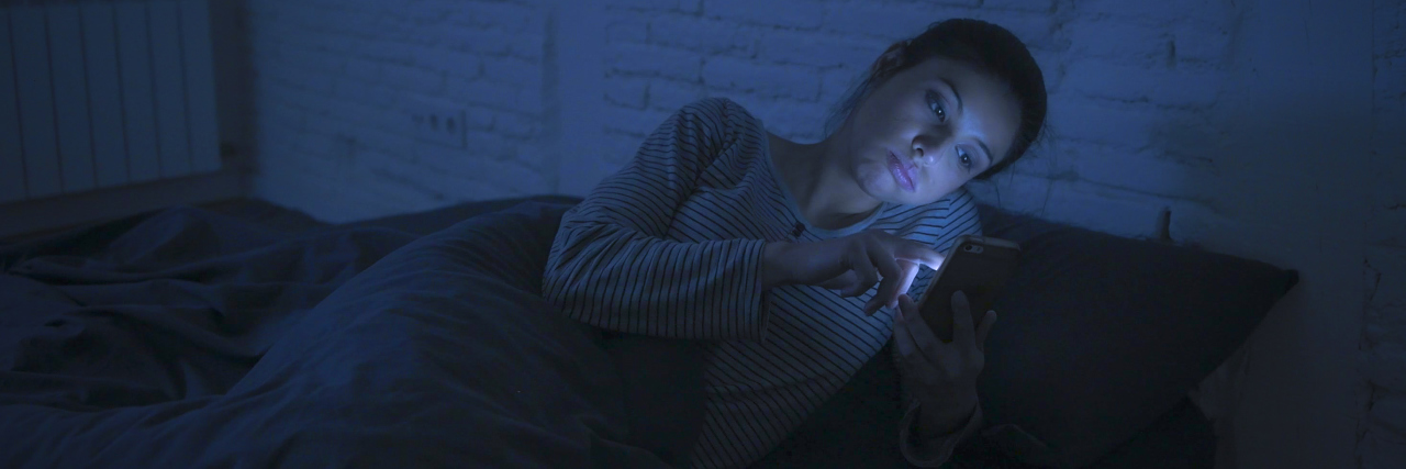woman lying in bed looking at her phone