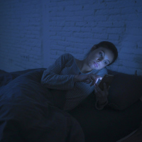 woman lying in bed looking at her phone