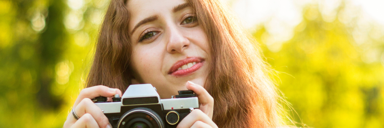 A young woman holding a camera, while she smiles.