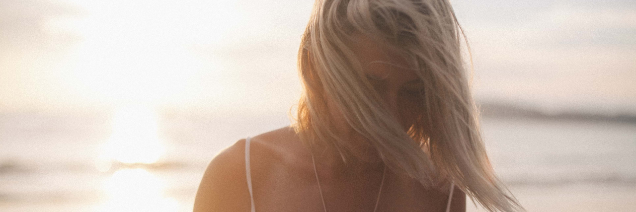 A picture of a woman in front of the beach, with her hair blowing in her face.