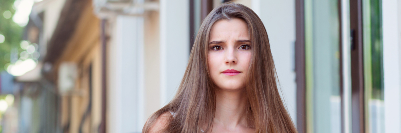 Mast Cell Activation Syndrome Makes Me Feel Cut Off From the World A young female standing outside with a serious expression on her face.