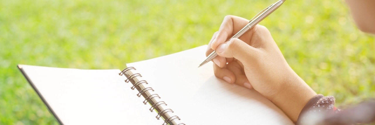 How to Reduce Stress When You Have a Rare, Chronic Illness close up of someone writing in a notebook on the grass