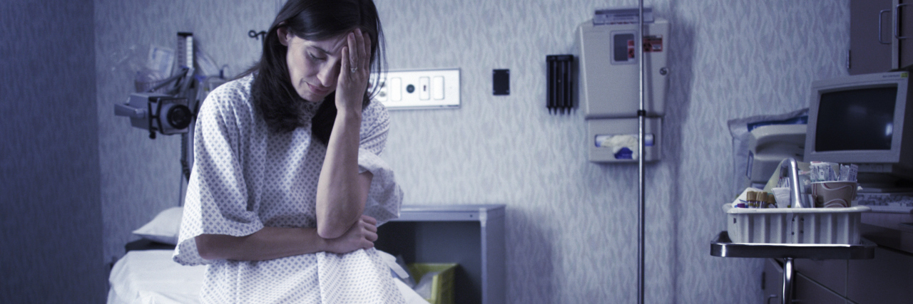 How Healthcare Providers Can Help Save Suicidal Patients Lives a concerned caucasian female patient dressed in a hospital gown sits in an exam room and looks worried