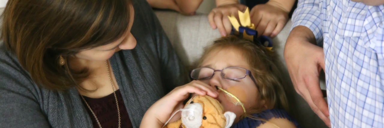 How My Daughter's Complex Medical Needs Affected My Marriage Family of 5. Parents and two boys all looking down at little girl in the middle who seems to be sleeping and has a disability