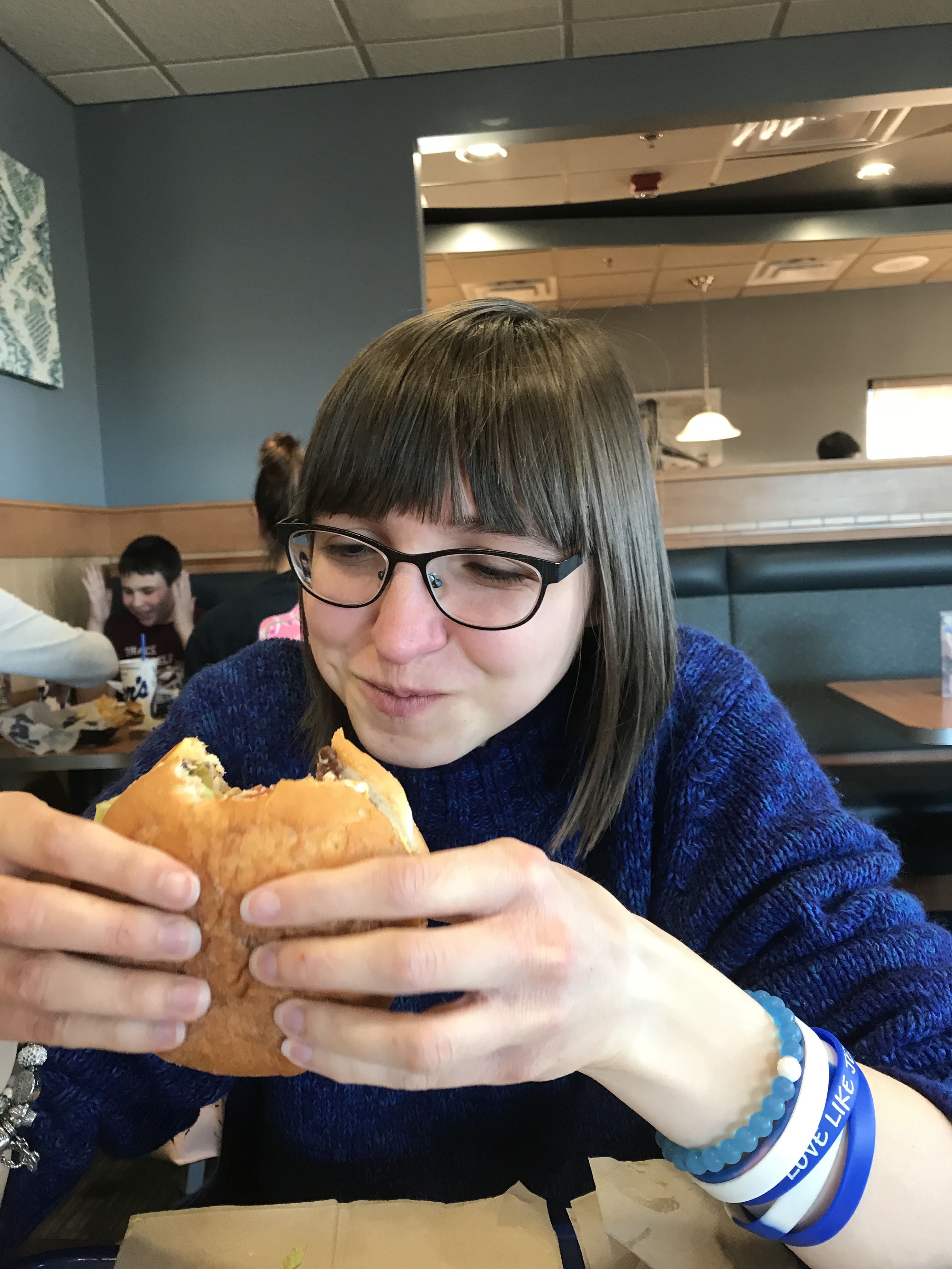 A picture of the writer looking at a cheese burger, with one bite already taken out.