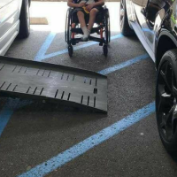 Image of a handicap accessible van with the ramp out with a car parked on the stripped loading area. A oung child sits between the cars showing it is impossible for him to access the ramp into his vehicle because of the car blocking access to the ramp