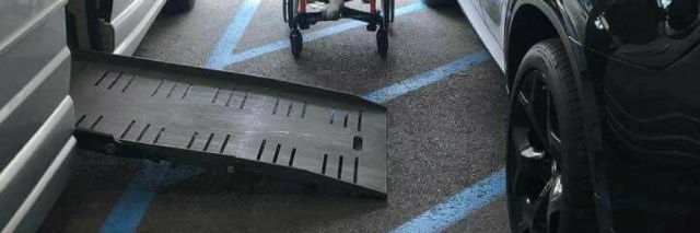 Image of a handicap accessible van with the ramp out with a car parked on the stripped loading area. A oung child sits between the cars showing it is impossible for him to access the ramp into his vehicle because of the car blocking access to the ramp